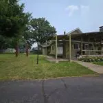 A single-story building with a covered porch, surrounded by grass and trees, with a large bell structure on the lawn to the left—celebrating 100 Years of tradition at Fred Thomas Resort. - Rice Lake Chamber of Commerce