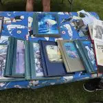 Several photo albums and scrapbooks are displayed on a table covered with a patterned cloth at an outdoor event, some open to show photos and documents highlighting 100 Years of memories at Fred Thomas Resort. - Rice Lake Chamber of Commerce