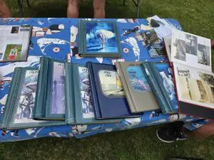 Several photo albums and scrapbooks are displayed on a table covered with a patterned cloth at an outdoor event, some open to show photos and documents highlighting 100 Years of memories at Fred Thomas Resort. - Rice Lake Chamber of Commerce