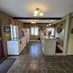 A small shop interior at Fred Thomas Resort, celebrating 100 Years, features tiled floors, a counter with shelves, a freezer, a refrigerator, wall decorations, and windows with plaid curtains. - Rice Lake Chamber of Commerce