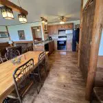 A rustic kitchen and dining area with wooden furniture, tile backsplash, black appliances, and lantern-style ceiling lights on a wood floor—perfect for enjoying 100 years of tradition at Fred Thomas Resort. - Rice Lake Chamber of Commerce