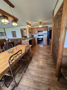 A rustic kitchen and dining area with wooden furniture, tile backsplash, black appliances, and lantern-style ceiling lights on a wood floor—perfect for enjoying 100 years of tradition at Fred Thomas Resort. - Rice Lake Chamber of Commerce