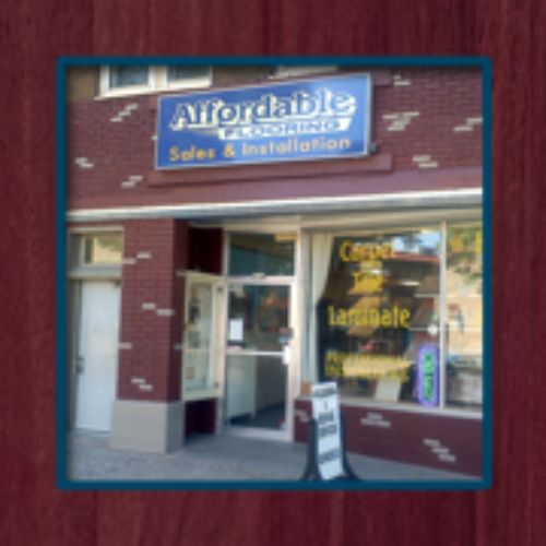 The storefront of a business named "Affordable Flooring" showcases signs indicating sales and installation for carpet and laminate flooring. The entrance is open, warmly welcoming customers, while a promotional sign is prominently displayed outside. - Rice Lake Chamber of Commerce