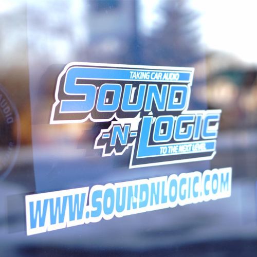 Sticker on a window displaying the logo of "Sound-N-Logic" with the tagline "Taking Car Audio to the Next Level" and their website www.soundnlogic.com. Integrate premium sound with unmatched logic for a superior car audio experience. - Rice Lake Chamber of Commerce