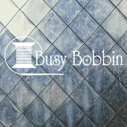 Logo for "Busy Bobbin" featuring a spool of thread and a needle, all set against a beautifully textured, patterned background. - Rice Lake Chamber of Commerce
